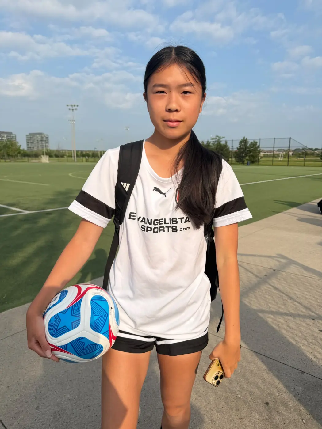 Angelina holding a soccer ball beside an outdoor field